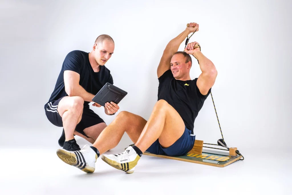 Mann trainiert an Dewboard Pro smart, Trainer liest Ergebnisse auf einem Monitor ab